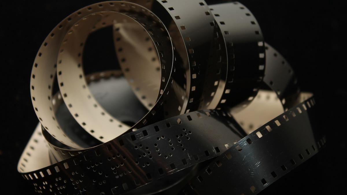 A length of 35mm film is coiled against a dark background, showing sprocket holes and frames. The film's reflective surface catches the light, highlighting its texture.
