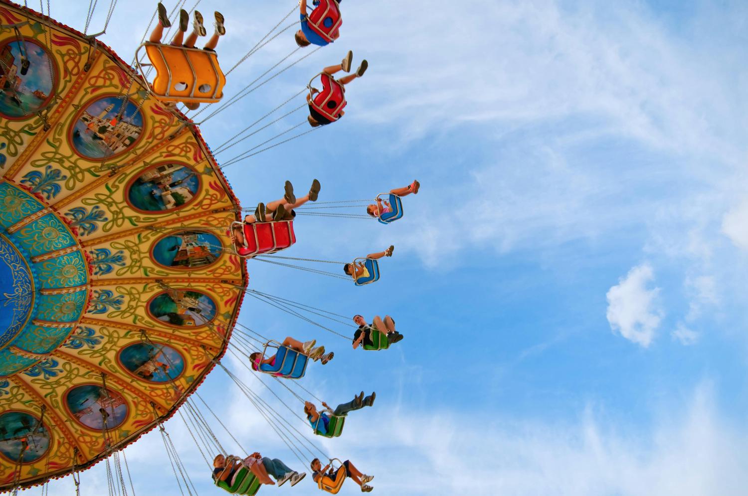People are enjoying a colorful swing ride against a backdrop of a blue sky with light clouds. The ride has decorative painted panels.