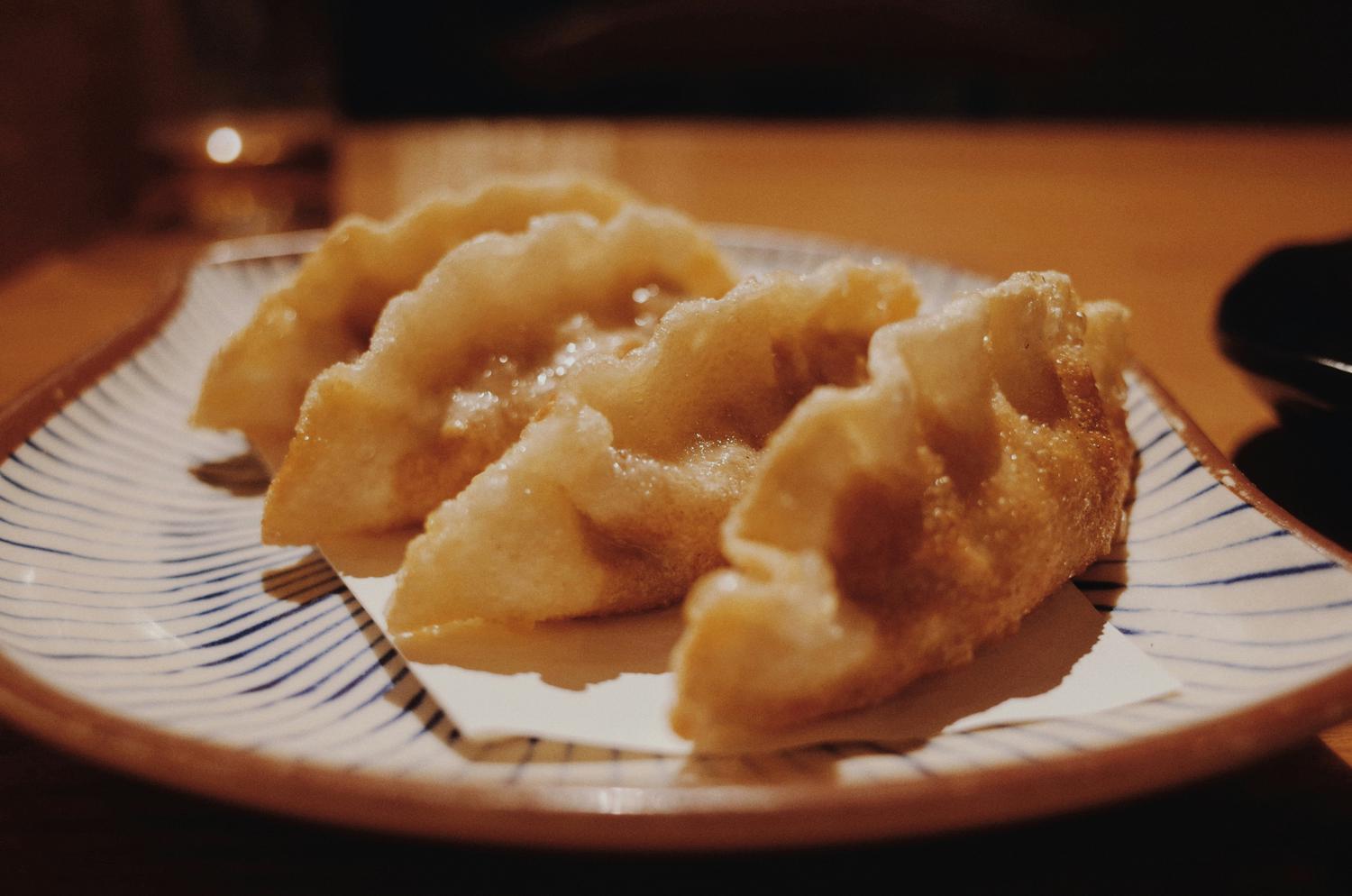 Close-up of golden-brown fried dumplings arranged on a white plate with a blue striped pattern. The dumplings appear crispy and juicy, ready to be enjoyed.