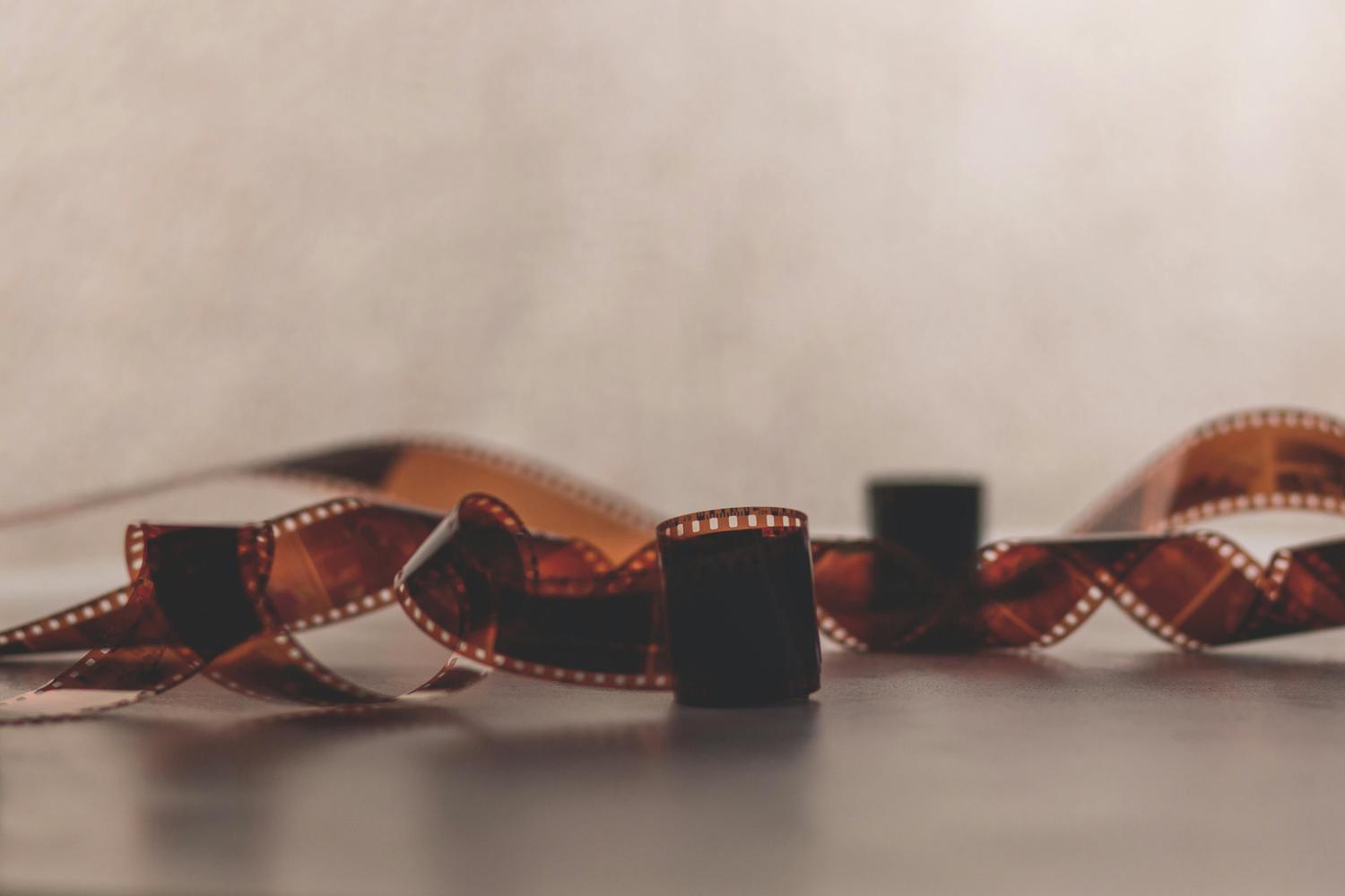 A strip of curled 35mm film rests on a light gray surface, with several frames visible showing dark images. The film is positioned in the center with out-of-focus background.
