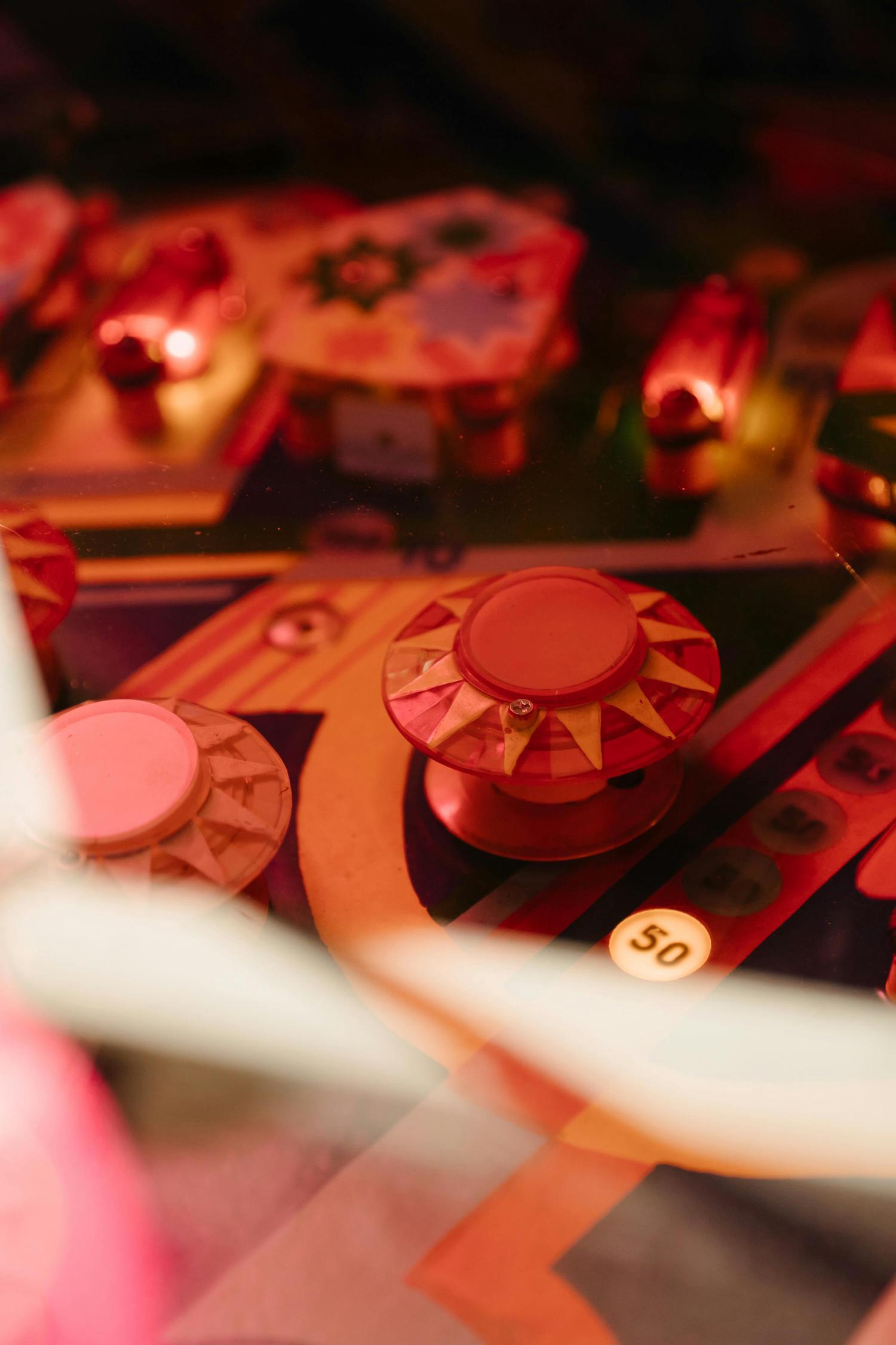A close-up view of a pinball machine's playfield shows targets and bumpers in red, orange, and yellow tones. The playfield has a glossy finish, with some lighting effects visible.