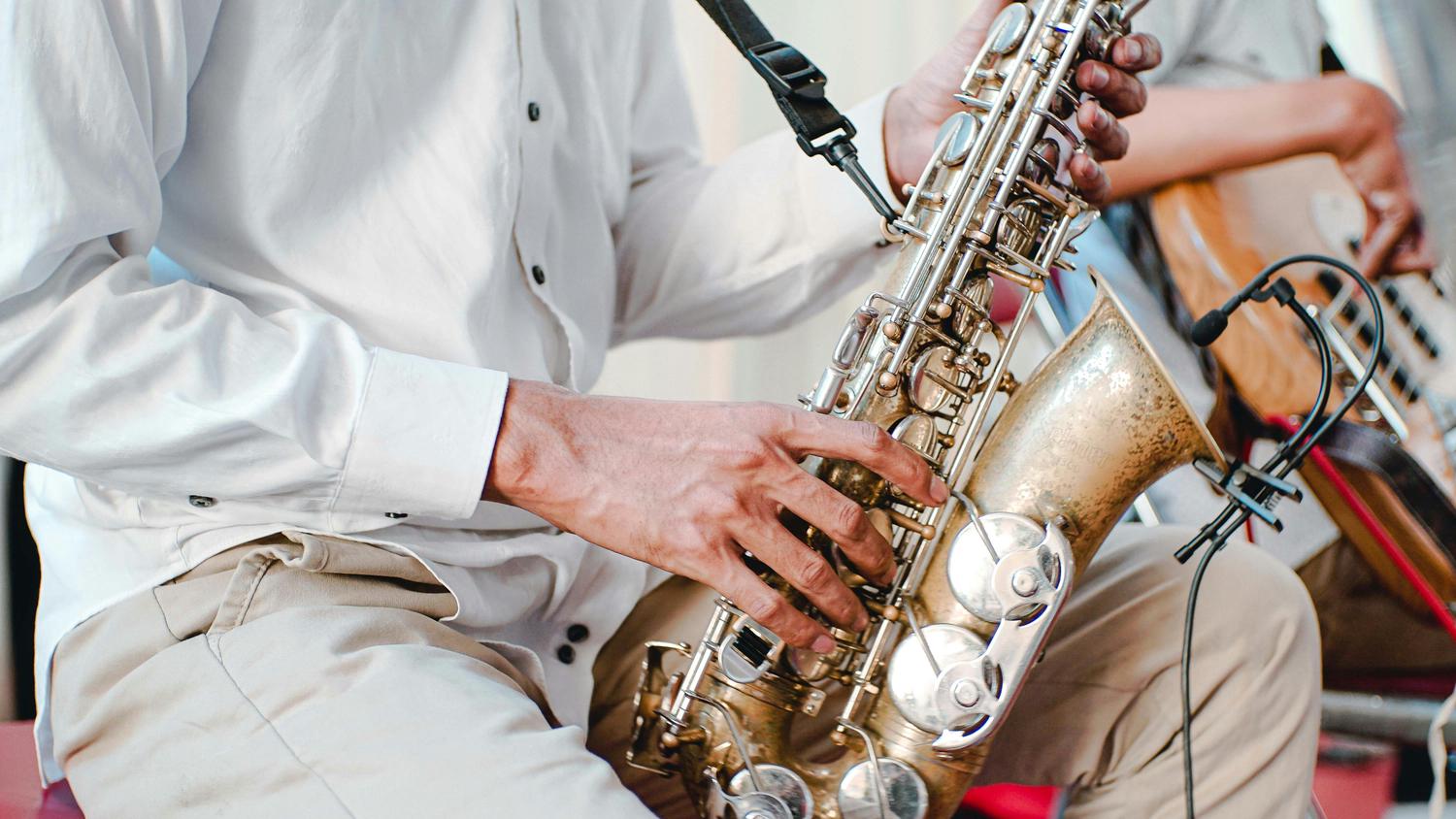A musician's hands press keys on a gleaming brass saxophone during a performance, with a microphone attached to the instrument.