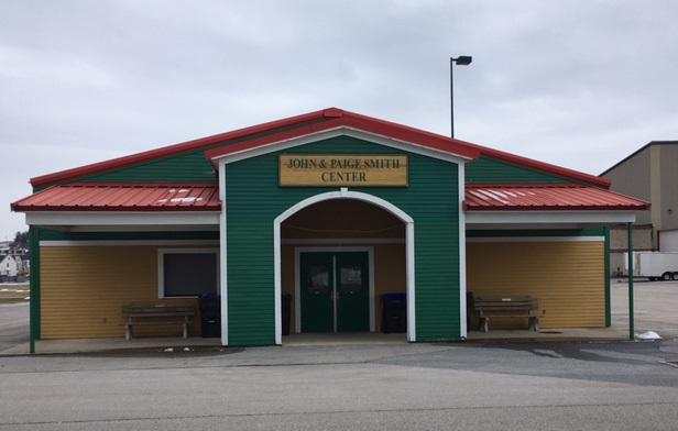 A colorful John & Paige Smith Center building with a bright red roof, green siding on top, and yellow siding below, features an arched main entrance flanked by two wooden benches.