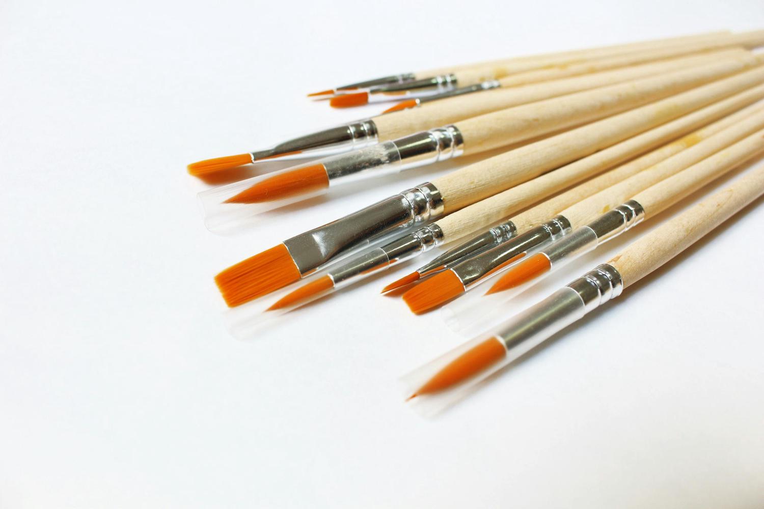 A collection of new paintbrushes with light wooden handles and vibrant orange synthetic bristles, some covered with clear protective caps, fanned out on a white background.