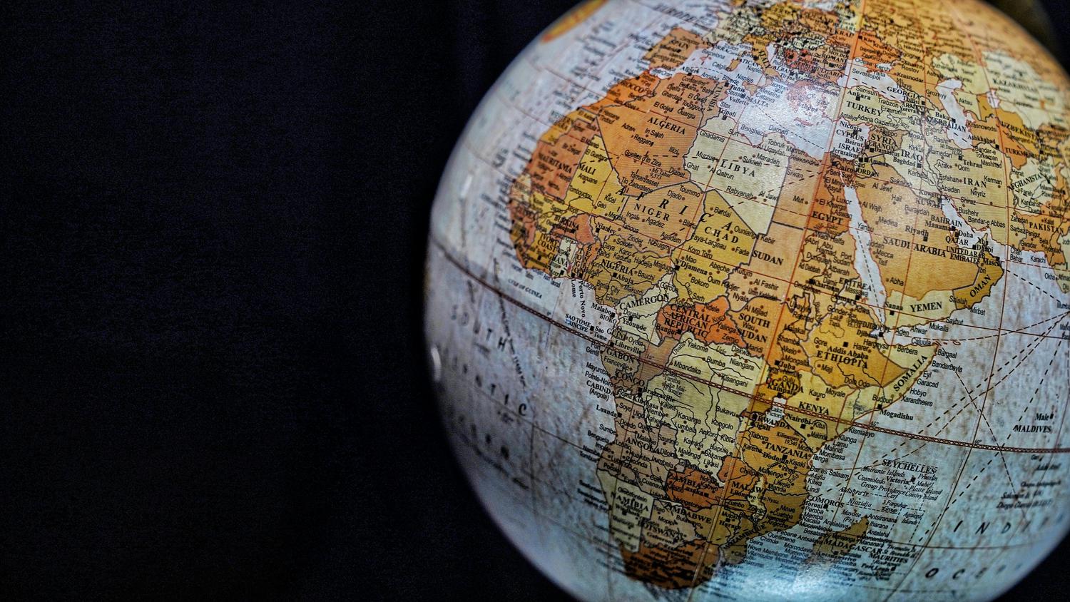 A detailed close-up of a vintage-style globe, prominently featuring Africa, parts of Europe, and the Middle East with visible country and city names against a dark background.