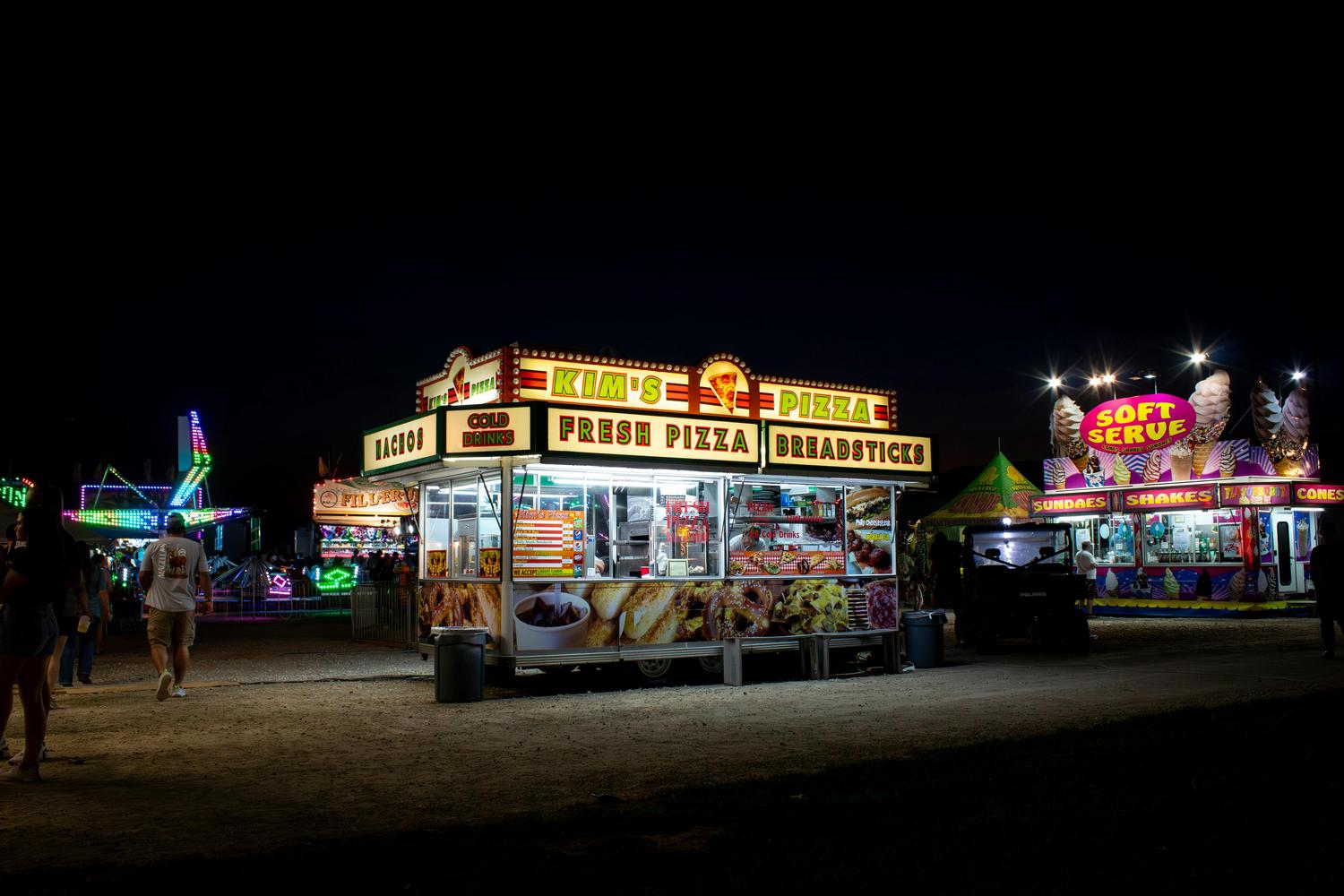A vibrant nighttime fair scene with brightly lit food trucks, including 
