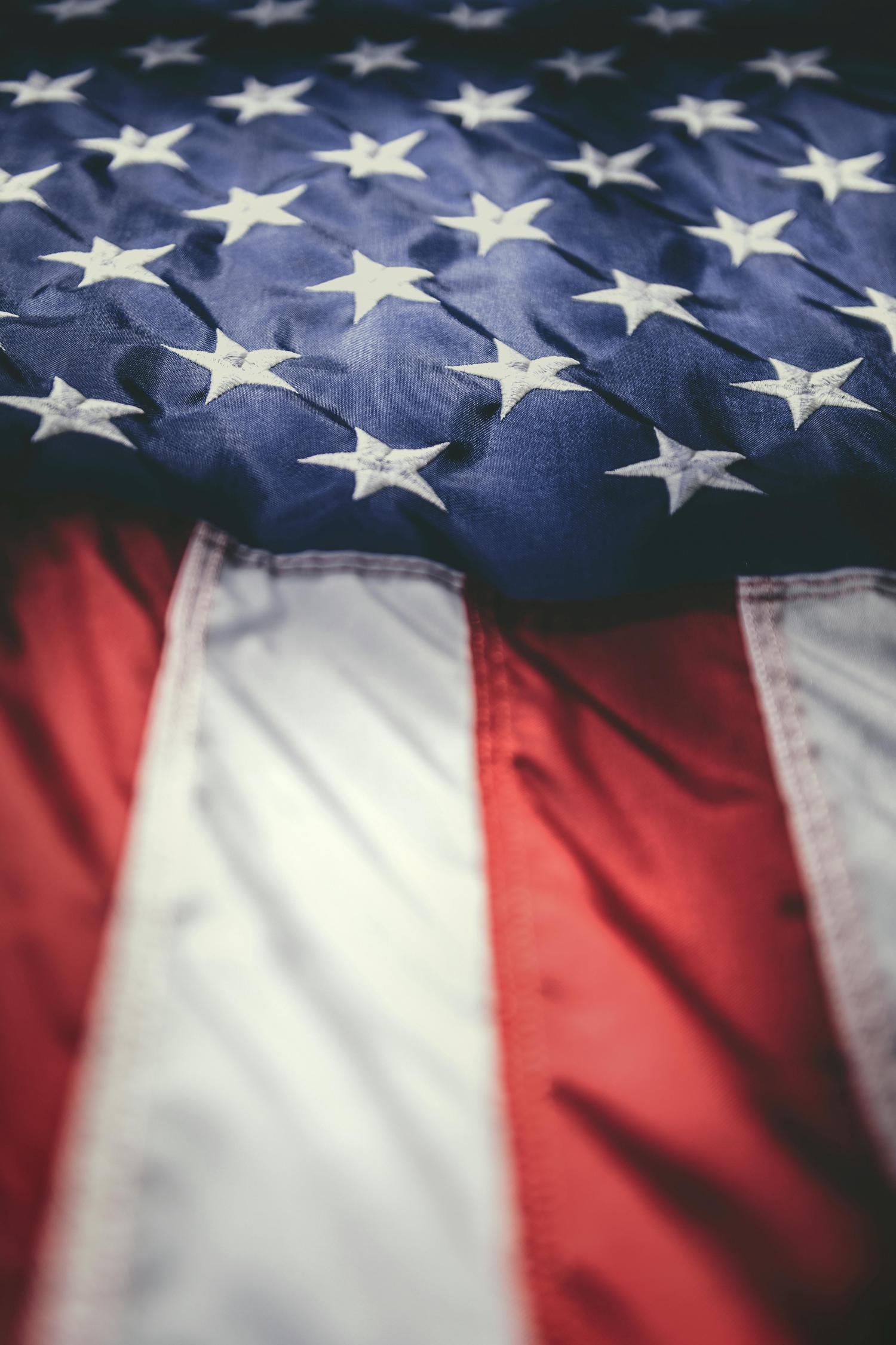A close-up of a textured American flag, showing the blue field with white stars at the top, and blurred red and white stripes below.