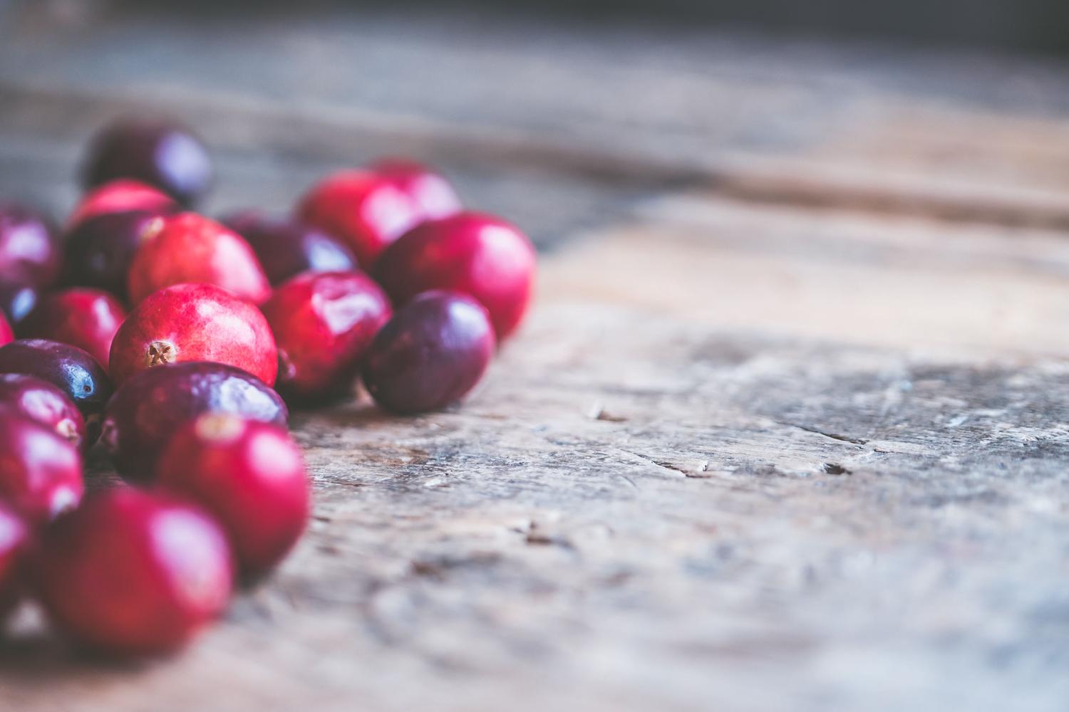 A cluster of vibrant red and deep purple cranberries rests on a weathered wooden surface.