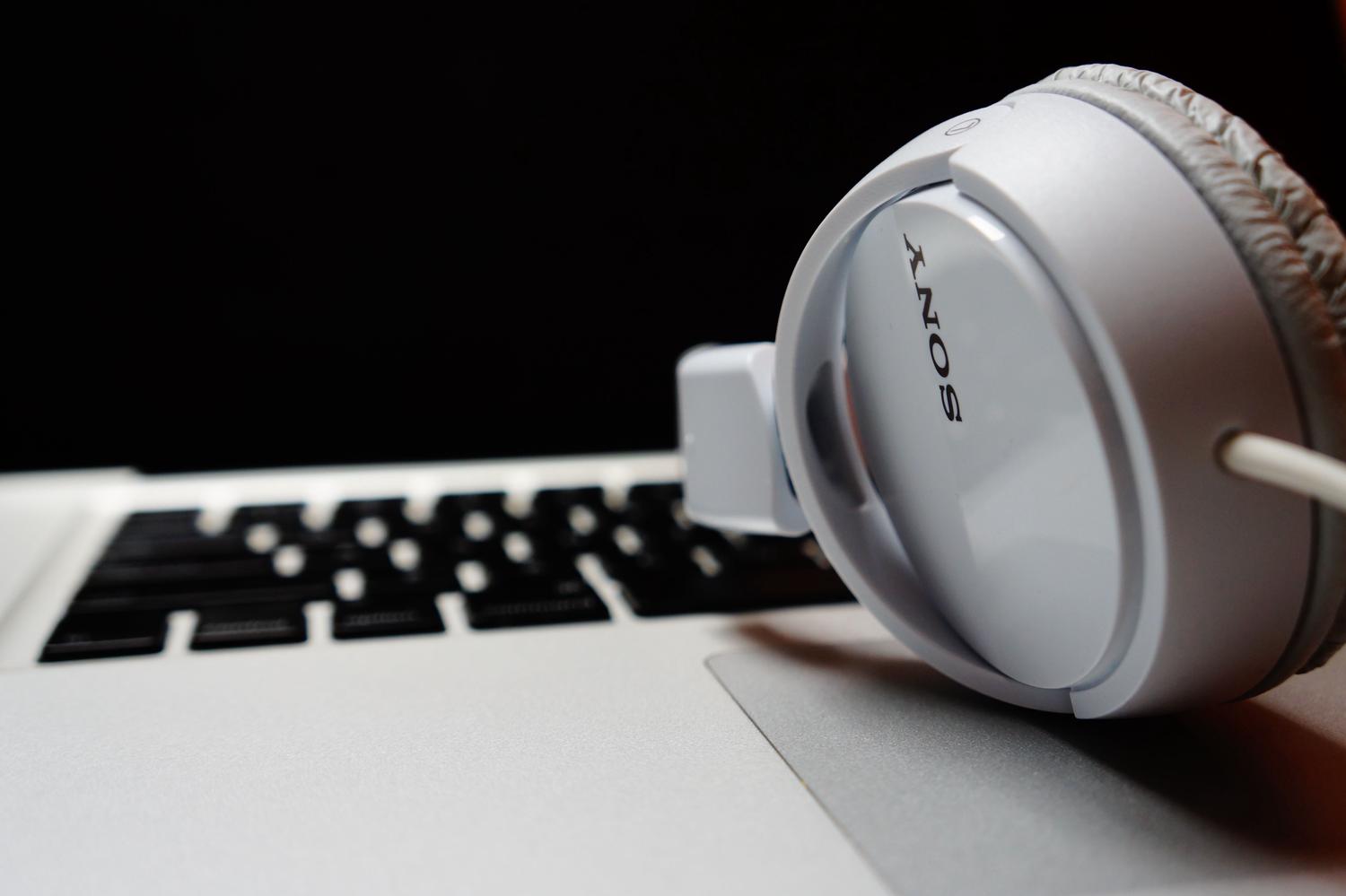 A white Sony headphone cup with its logo visible rests on a silver laptop keyboard, against a dark background.