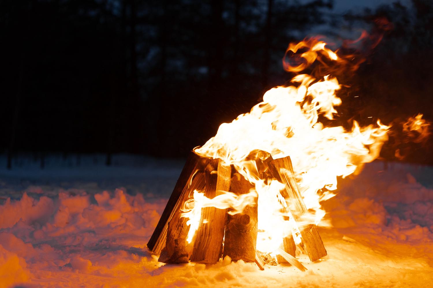 A bonfire burns against a dark, twilight sky with the sea visible on the left; sparks fly upwards in a shower of light.