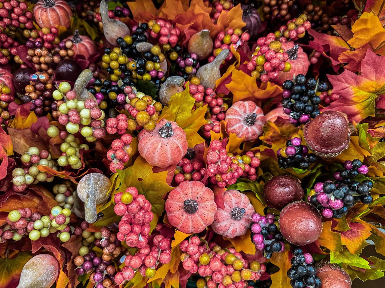 A dense autumn decoration features small textured peachy-pink pumpkins, clusters of red, yellow, green, black, and purple berries, alongside vibrant fall leaves. This festive arrangement captures the essence of harvest season.